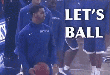 a man in a kentucky jersey is holding a basketball in front of a sign that says let 's ball