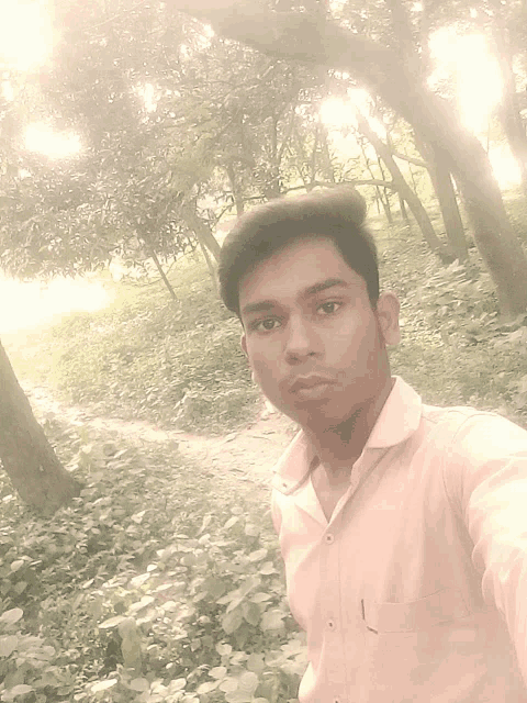 a young man in a pink shirt is taking a selfie in a forest