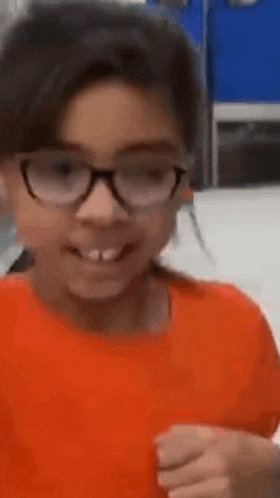 a young girl wearing glasses and an orange shirt is smiling and looking at the camera .