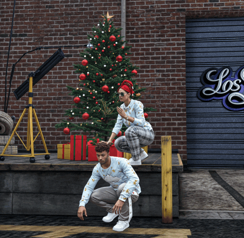 a man and a woman squatting in front of a christmas tree in front of a sign that says los