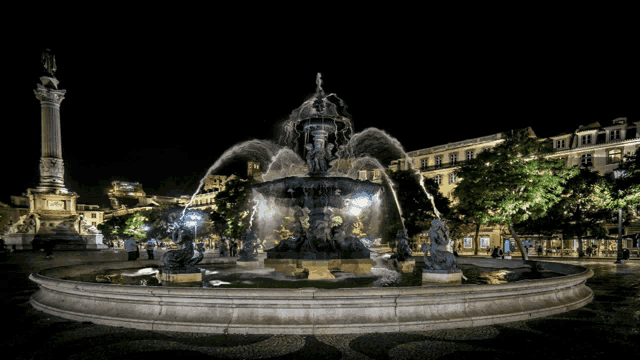 a fountain is lit up at night with a statue in the background that says ' a ' on it