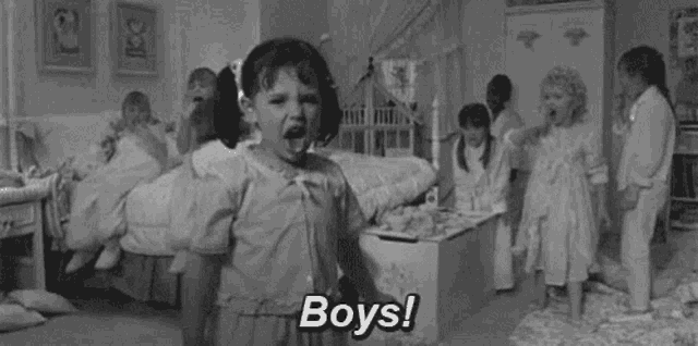 a black and white photo of a little girl standing in front of a group of children in a bedroom .