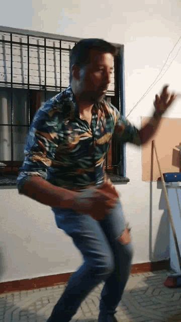 a man in a hawaiian shirt and jeans is dancing in front of a window