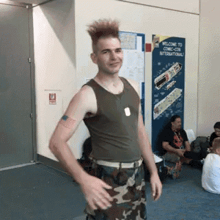 a man in a tank top and camo pants is standing in front of a welcome to comic con international sign