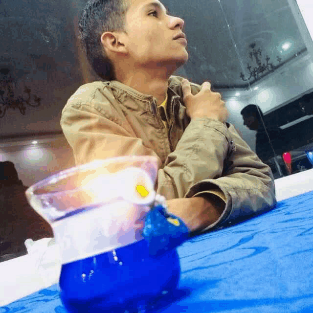 a young man is sitting at a table with a blue container on it