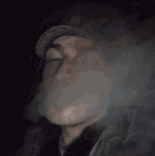 a man in a hat is smoking a cigarette and smoke is coming out of his mouth