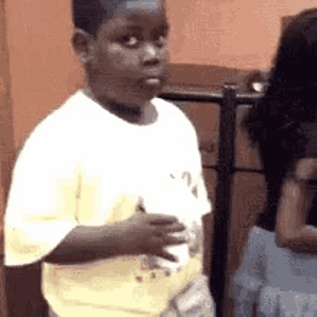 a young boy in a yellow shirt is standing in a room holding a piece of paper .