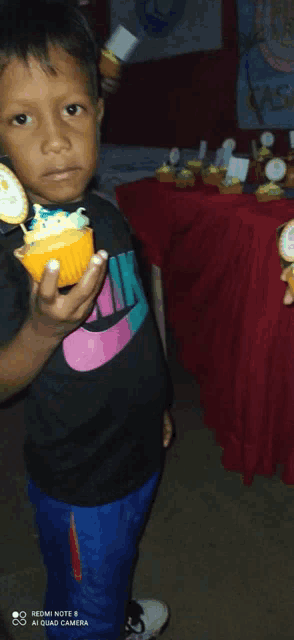 a young boy wearing a black nike shirt holds a cupcake in his hand