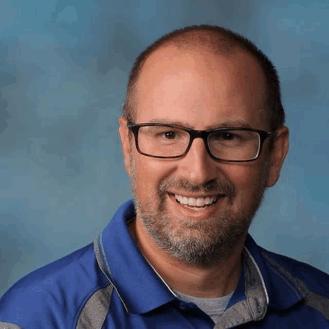 a man wearing glasses and a blue shirt is smiling .