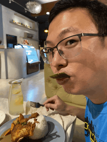 a man wearing glasses is eating a plate of food with a fork in his mouth