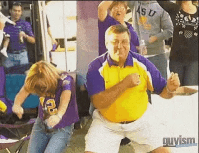 a man in a yellow shirt is dancing with a woman wearing a purple shirt with the number 12 on it .