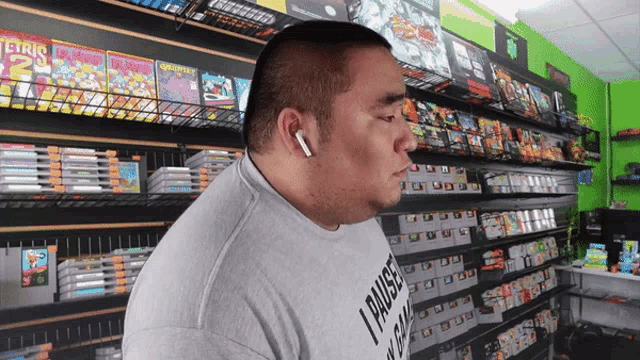 a man wearing a t-shirt that says " paused " is standing in front of a shelf full of video games