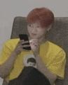 a young man with red hair is sitting in a chair looking at his phone .