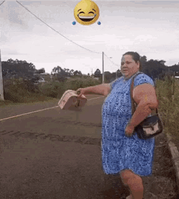 a woman in a blue dress is standing on the side of a road with a smiley face flying in the air behind her .