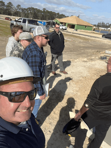 a group of men wearing hard hats and sunglasses are standing in a dirt field