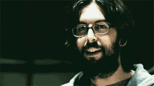 a man with glasses and a beard is smiling in a dark room