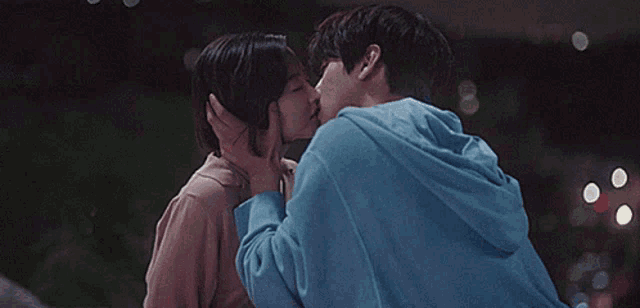 a man and a woman are kissing each other on the forehead . the man is wearing a blue hoodie .