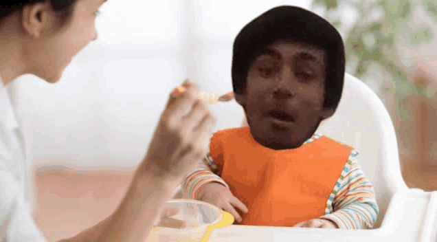 a baby in an orange bib is being fed by a woman with a spoon