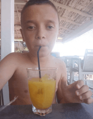 a shirtless boy drinks orange juice through a straw