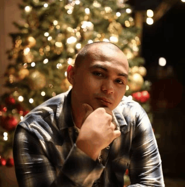 a man in front of a christmas tree with his hand on his chin