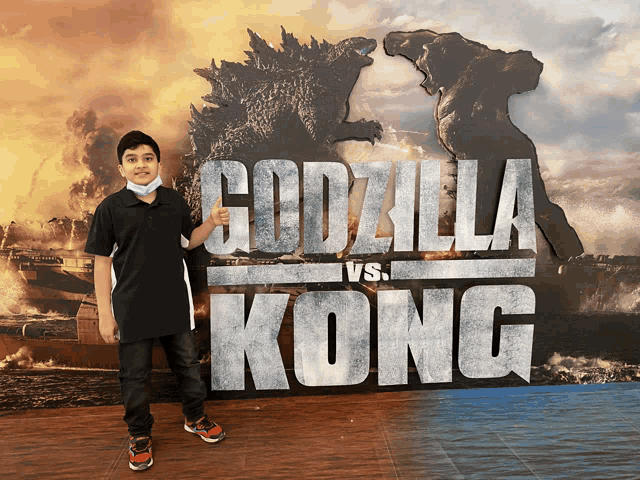 a young boy is standing in front of a poster for godzilla vs kong