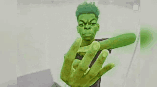 a man with green hair is holding a green object in his hand and giving the middle finger .