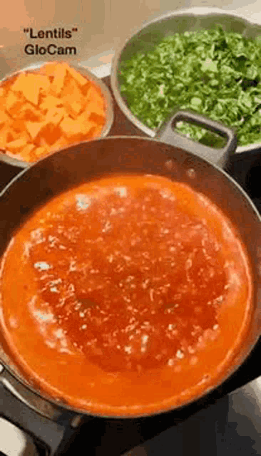 a pot of tomato sauce is being cooked in a pan on a stove next to bowls of vegetables .