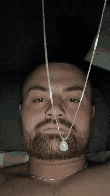 a man with a beard is laying down with two necklaces hanging from his neck