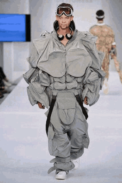 a model walks down the runway at a fashion show wearing headphones and goggles