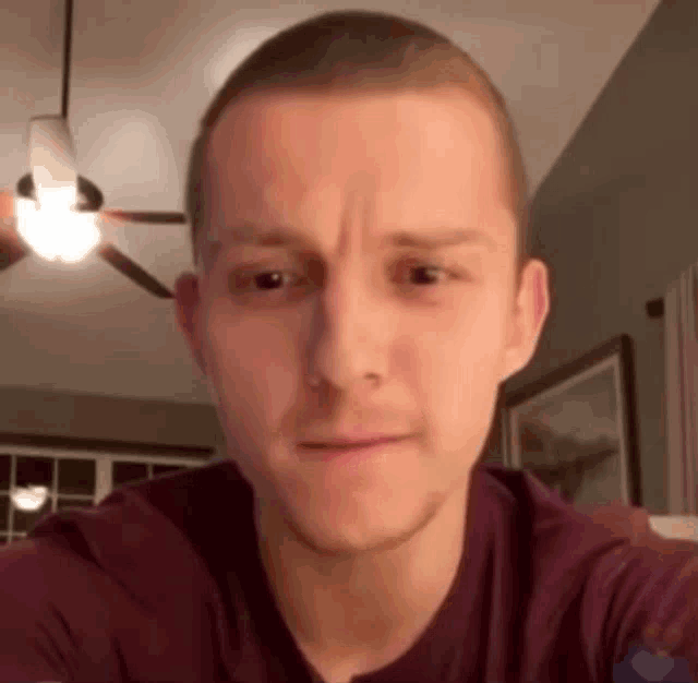 a man with a shaved head is looking at the camera in a room with a ceiling fan in the background .