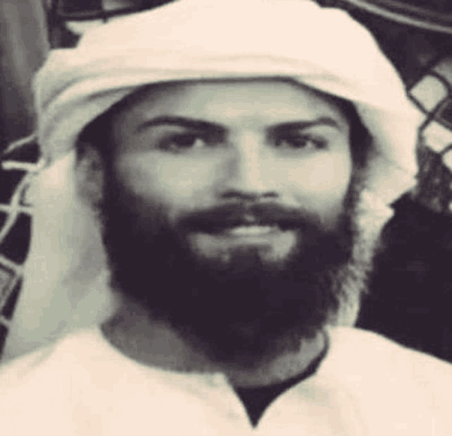 a black and white photo of a man with a beard wearing a white head scarf .