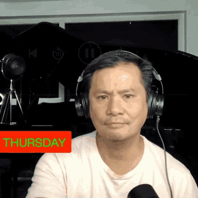 a man wearing headphones looks at the camera with a red sign that says thursday on it