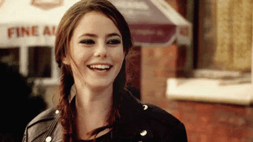 a woman wearing a leather jacket and braids is smiling in front of a fine a ice cream stand .