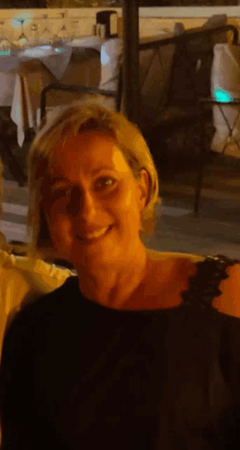 a woman in a black shirt is smiling in front of a restaurant table