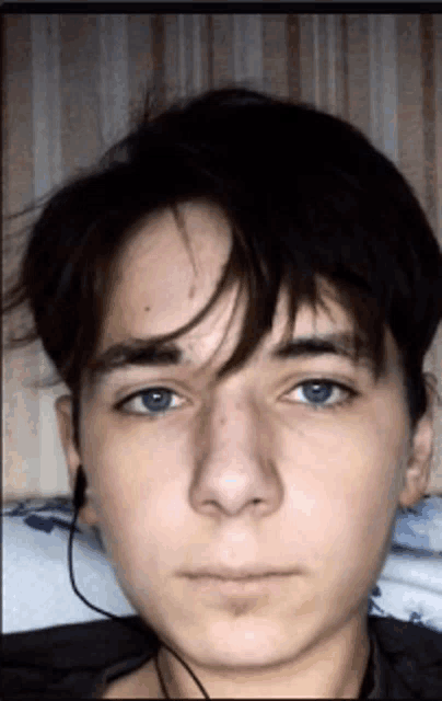 a young man with blue eyes is laying on a bed