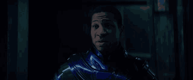 a man in a blue and green suit is standing in a dark room looking at the camera .