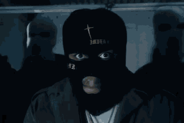 a man wearing a black ski mask with a cross and the word imperator on it