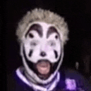 a close up of a person wearing a clown mask and a purple shirt .