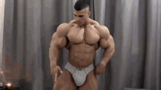 a muscular man in white underwear is standing in front of a grey curtain .