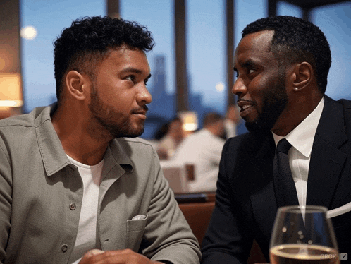 two men are sitting at a table with a glass of wine in front of them and the word cook on the bottom right