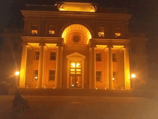 a large building is lit up at night and a person in a wheelchair is standing in front of it