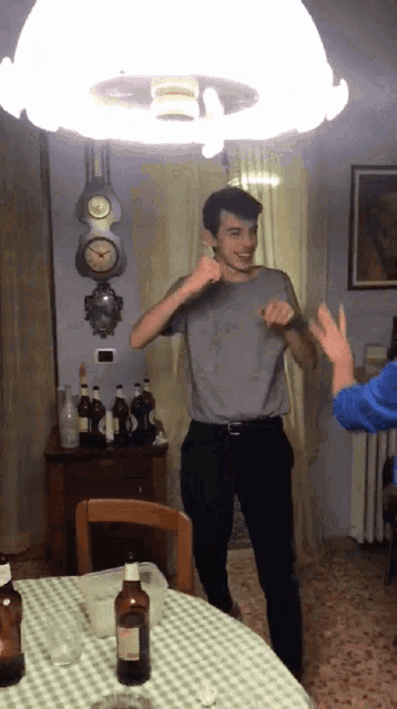 a man in a grey shirt is dancing in front of a table with a bottle of beer on it