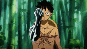 a shirtless monkey d luffy is standing in a forest holding his fist up .