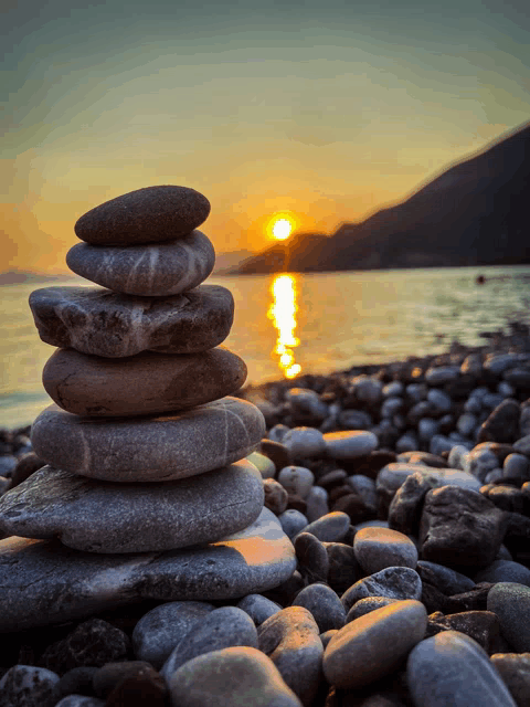 a stack of rocks on a beach with the sun setting in the distance