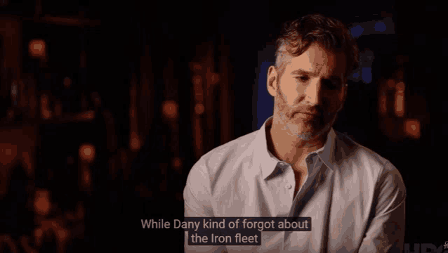 a man in a white shirt says " while dany kind of forgot about the iron fleet " in a dark room