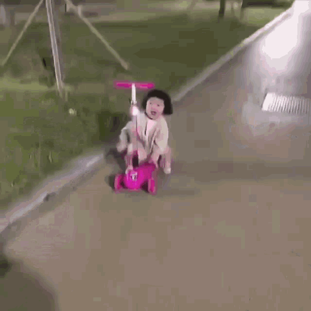 a little girl is sitting on a pink scooter on a sidewalk .