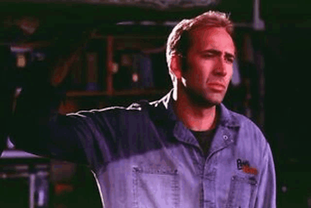 a man in a denim shirt is standing with his arms outstretched in a garage .