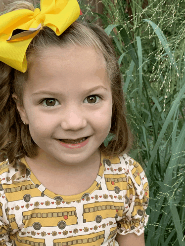 a little girl with a yellow bow in her hair wears a shirt with school buses on it