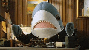 a stuffed shark is sitting at a desk wearing a suit .