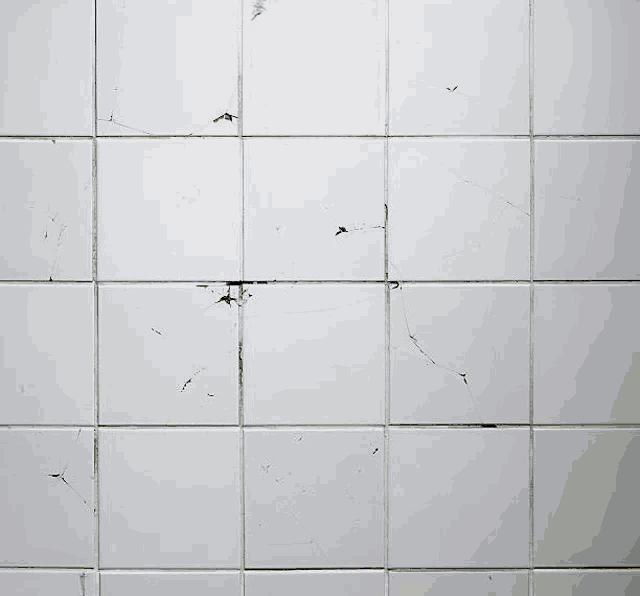 a white tile wall with a few cracks and stains